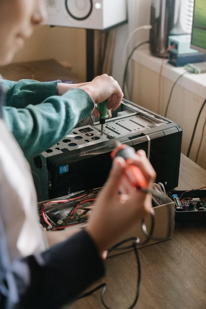 Adults working together to repair a computer using tools like a screwdriver and soldering iron.